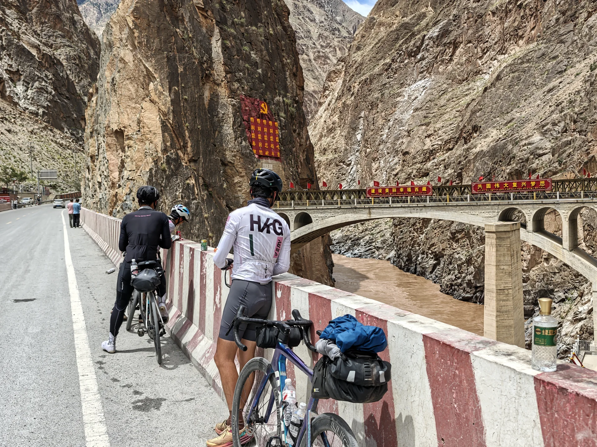 Cyclists walking their bikes across a bridge in a rocky gorge