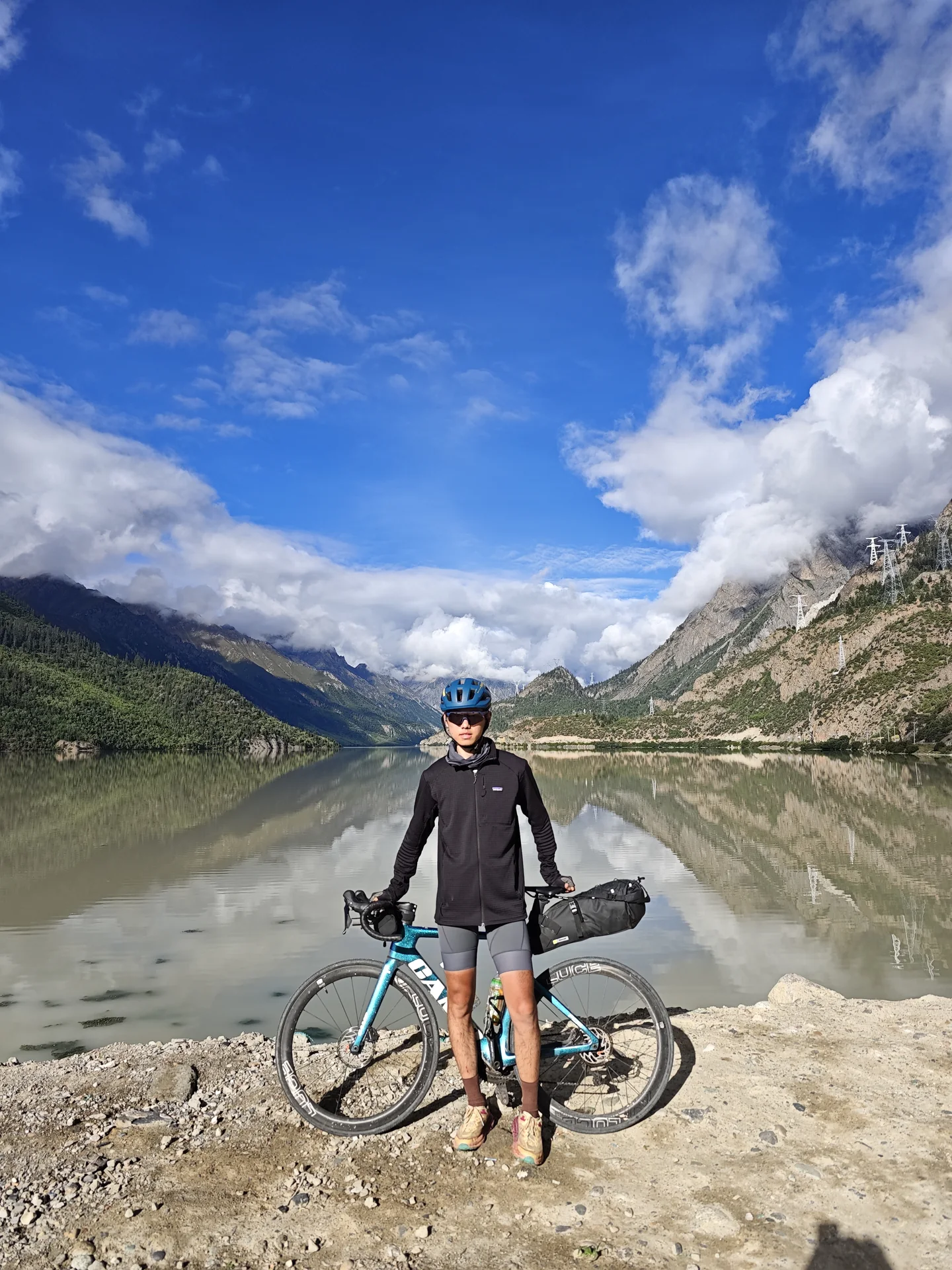A cyclist standing with a loaded bicycle on a rocky riverbank