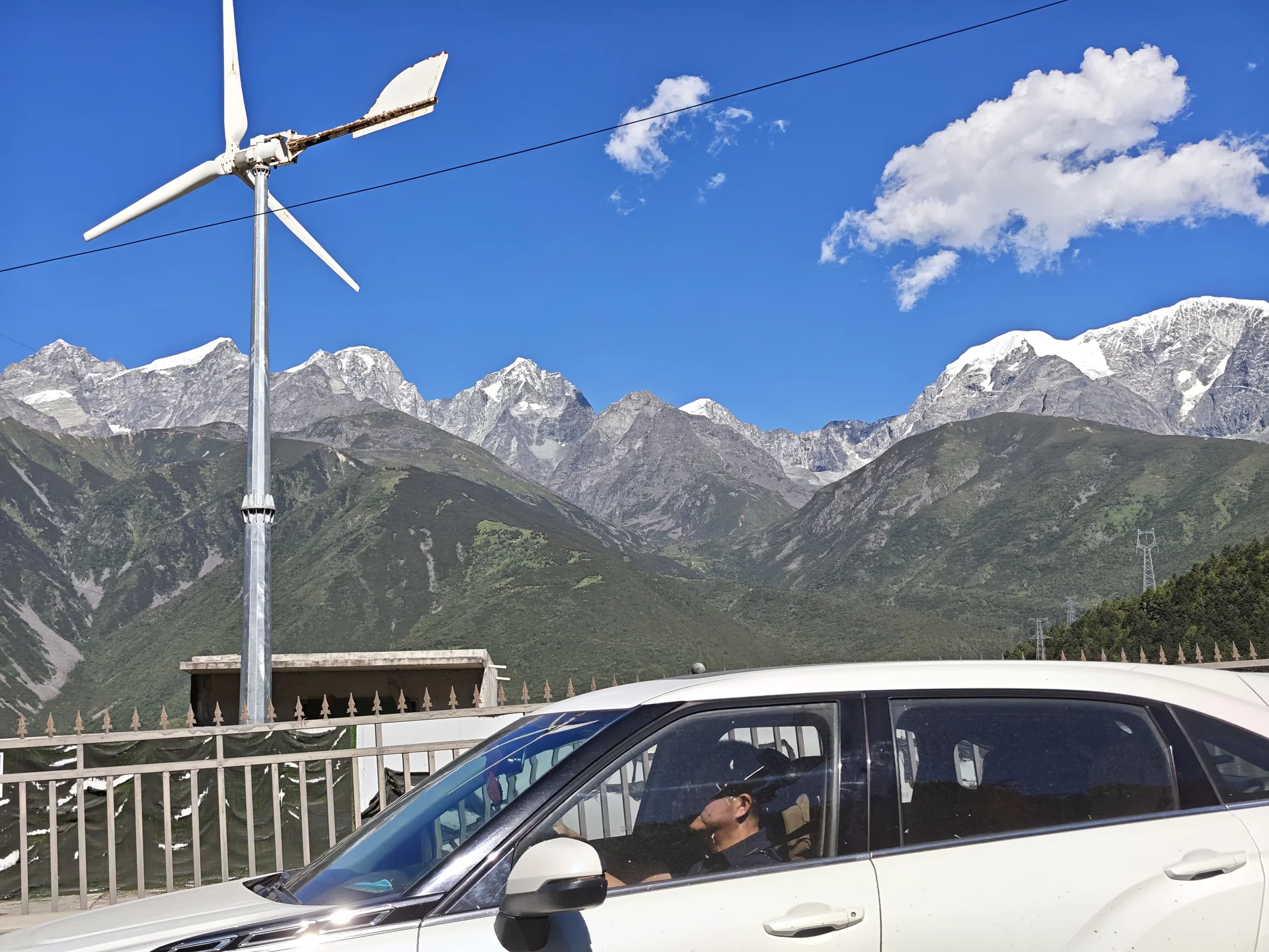 Wind turbines and a parked car beneath snowy peaks
