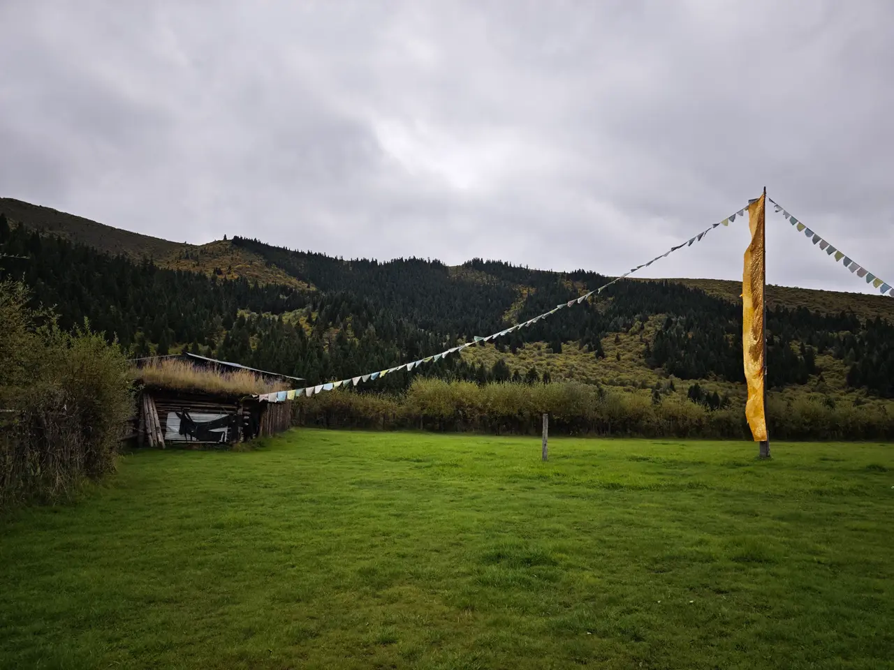 草地上的木屋和高高经幡立在谷口，像当天短暂停留的营地。