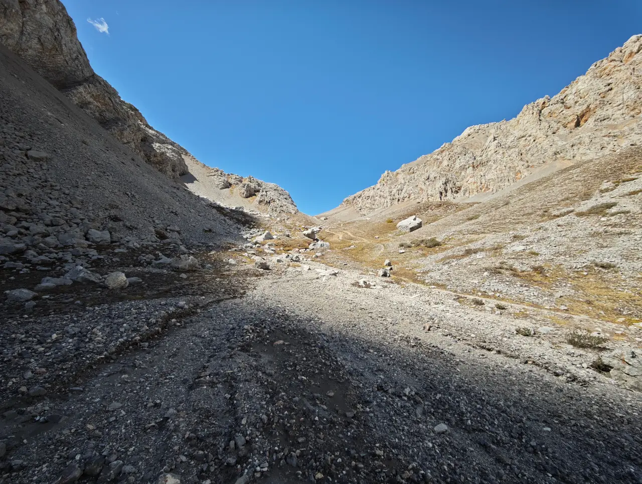 碎石路一路抬升进入裸岩山口，蓝天让地形的陡峭感更加直接。